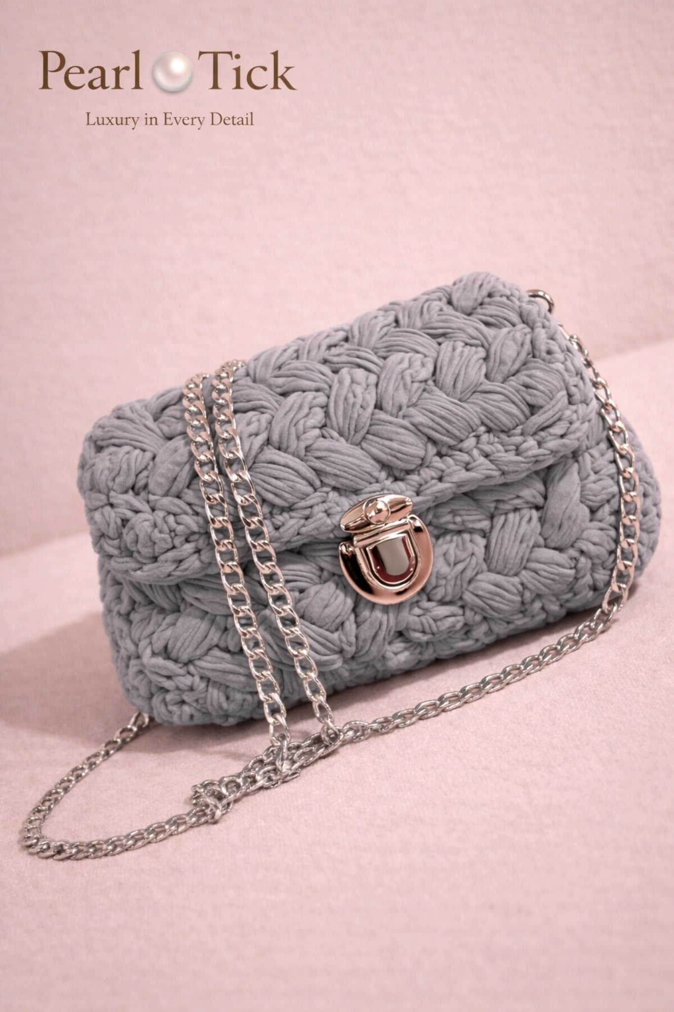 Borsa a mano intrecciata grigia con tracolla a catena su sfondo rosa, con il marchio 'Pearl Tick'.