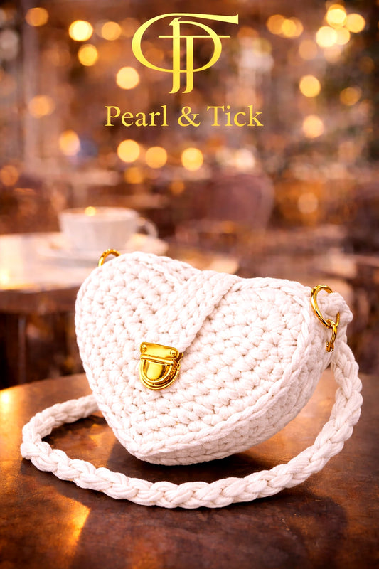 White woven handbag with gold accents on a wooden surface, blurred background with 'Pearl & Tick' branding.