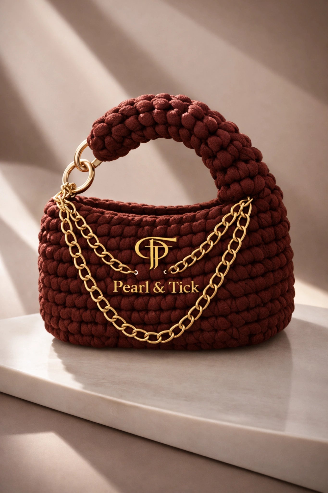 PT Knot Edition - Pearl & TickPT Knot EditionHandbagsPearl & TickPearl & TickKNOT-BRGBurgundyLuxurious Brown Handbag: Showcasing a refined gold chain handle against a minimalist light surface. An elegant piece that captures the essence of cinematic style and premium craftsmanship by Pearl & Tick.