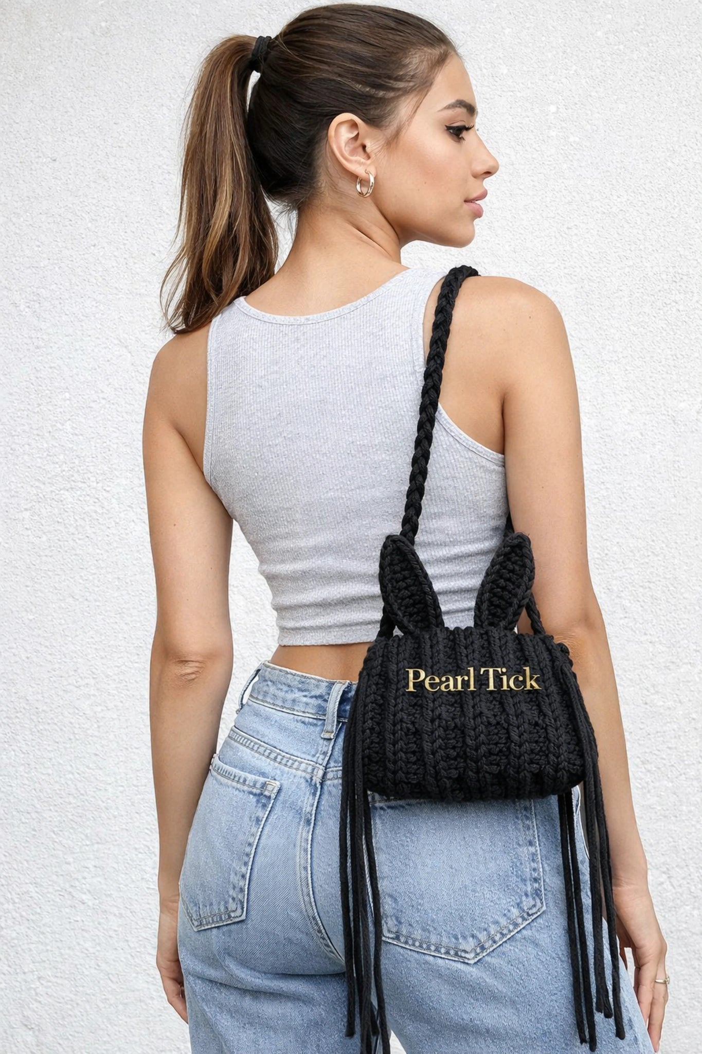 Woman carrying a black fringed handbag with 'Pearl Tick' branding against a light background