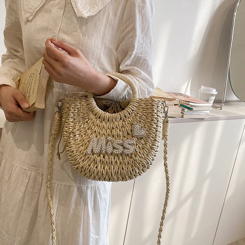 Person holding a woven handbag with 'MISS' embroidery in a casual setting.