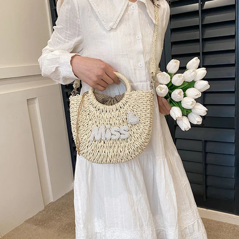 Person holding a woven handbag with 'MISS' text and a bouquet of white tulips.