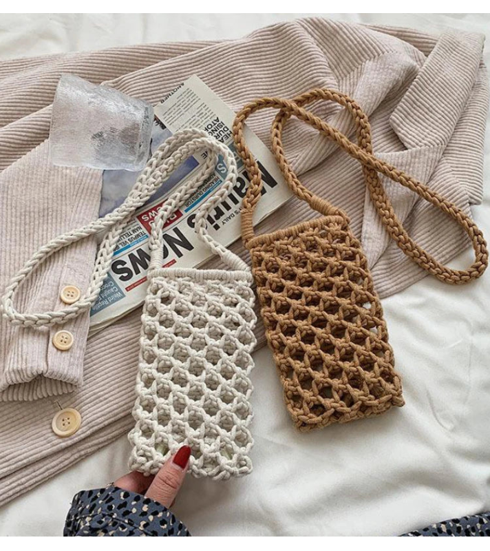 Deux sacs en crochet, un blanc et un marron, sur un lit avec un journal et des vêtements.