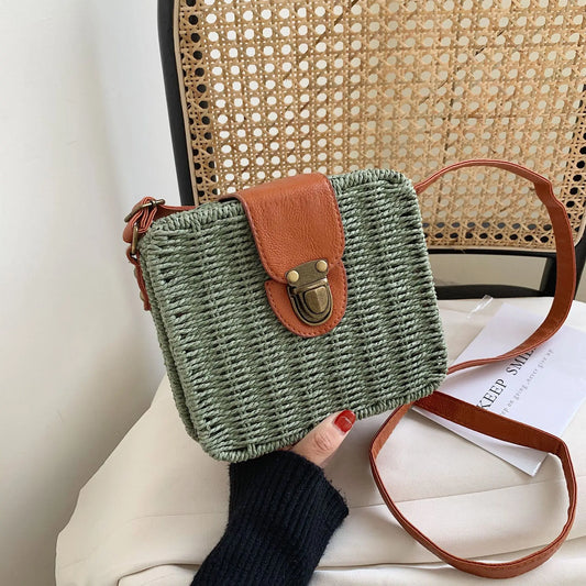 Borsa intrecciata verde con tracolla in pelle marrone, tenuta da una persona su una superficie bianca.