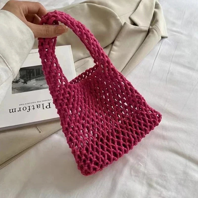 Sac à main tressé rose tenu par une main sur un fond clair