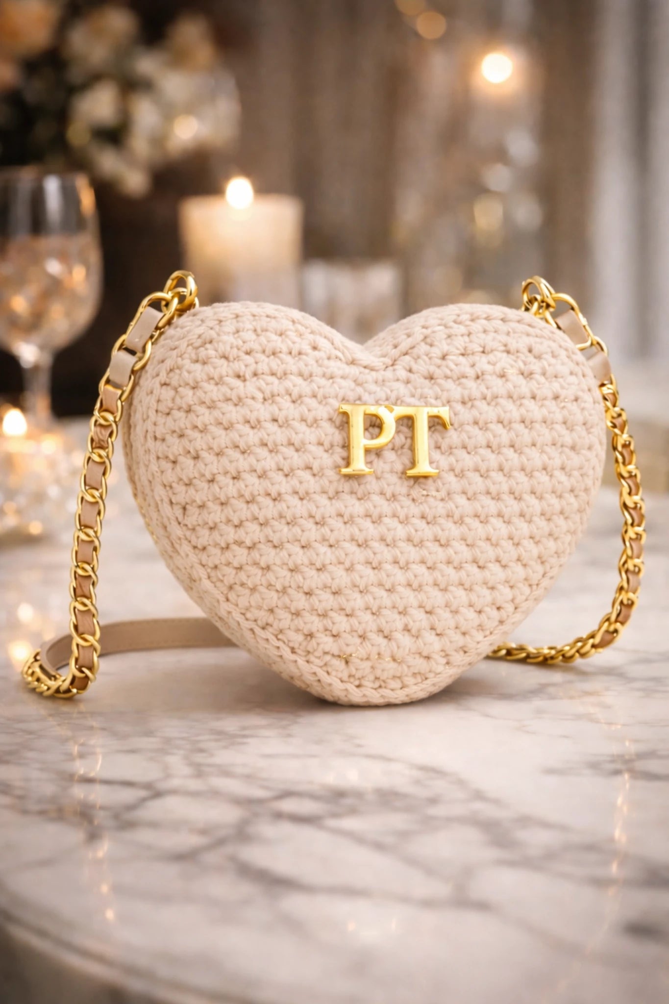 Sac en crochet en forme de cœur avec chaîne dorée et initiales 'PT' sur une surface en marbre.