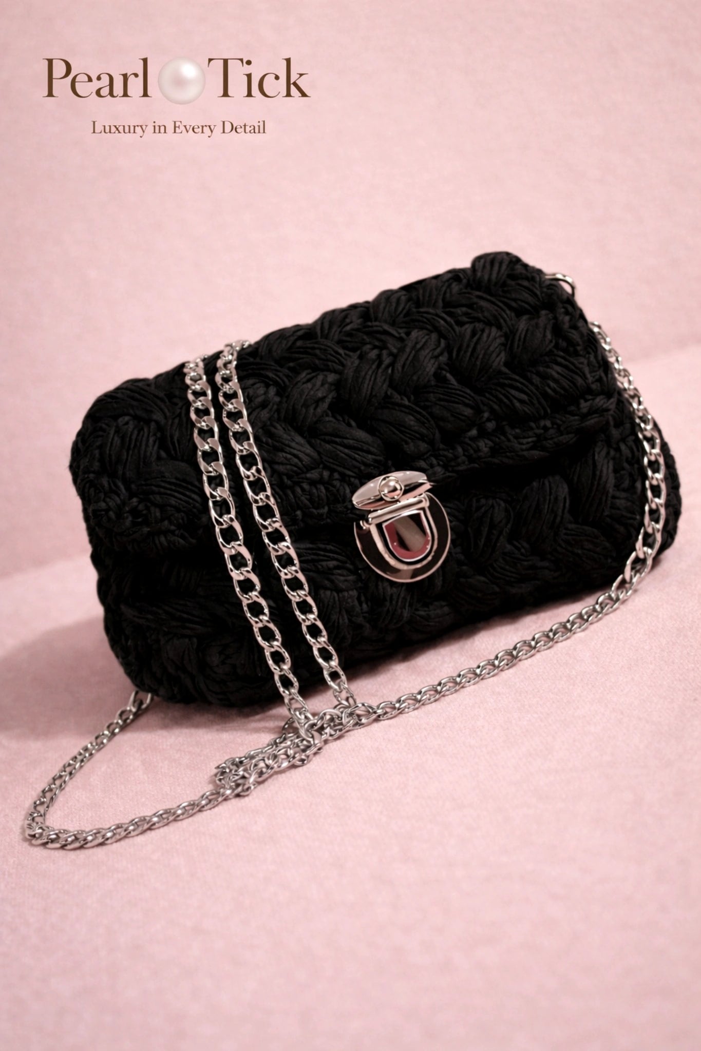 Black textured handbag with a chain strap on a pink background, featuring the brand 'Pearl Tick'.