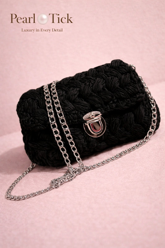Black textured handbag with a chain strap on a pink background, featuring the brand 'Pearl Tick'.