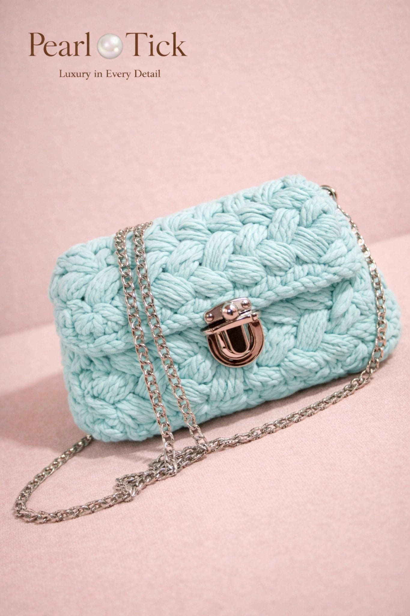 Light blue knitted handbag with a chain strap on a pink background, featuring the brand 'Pearl Tick'.