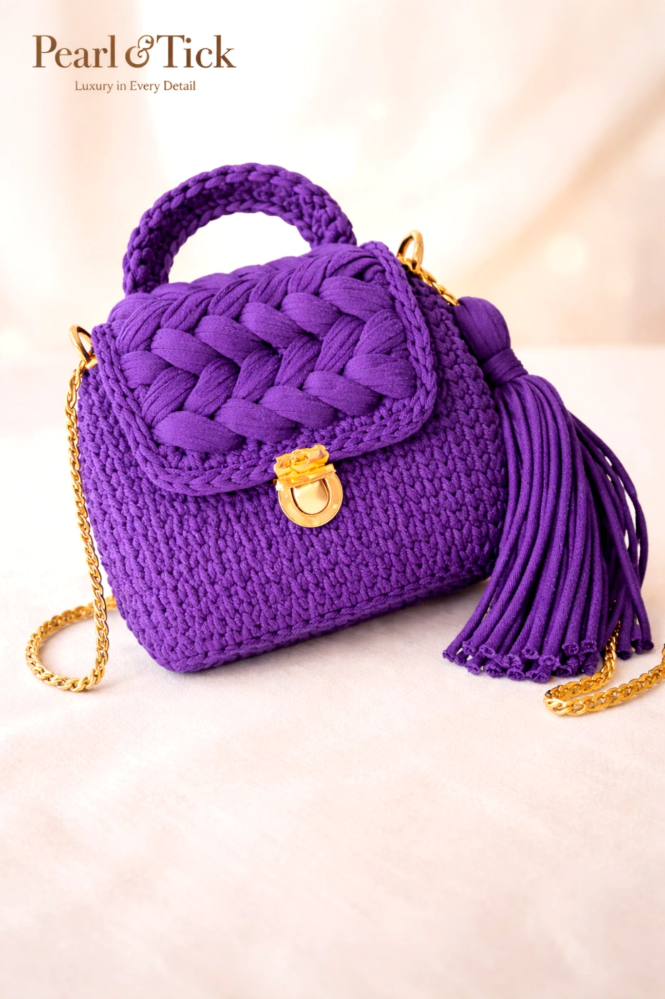 Borsa viola con motivo intrecciato e nappina su sfondo chiaro, con il marchio «Pearl & Tick».