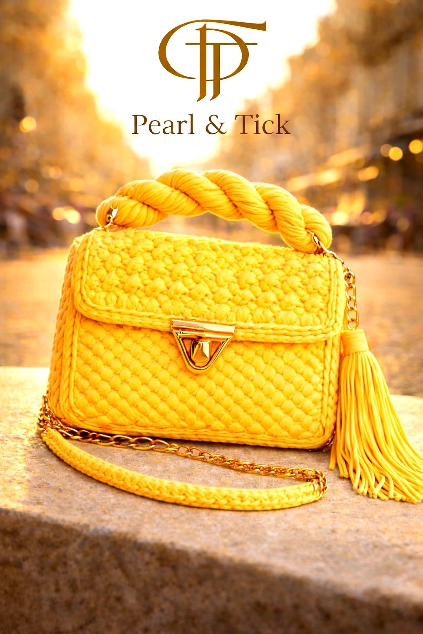 PT Golden Charm Bag - Pearl & TickPT Golden Charm BagHandbagsPearl & TickPearl & TickGOLDEN-YLWYellowYellow handbag with a tassel on a blurred street background, featuring the brand 'Pearl & Tick'.