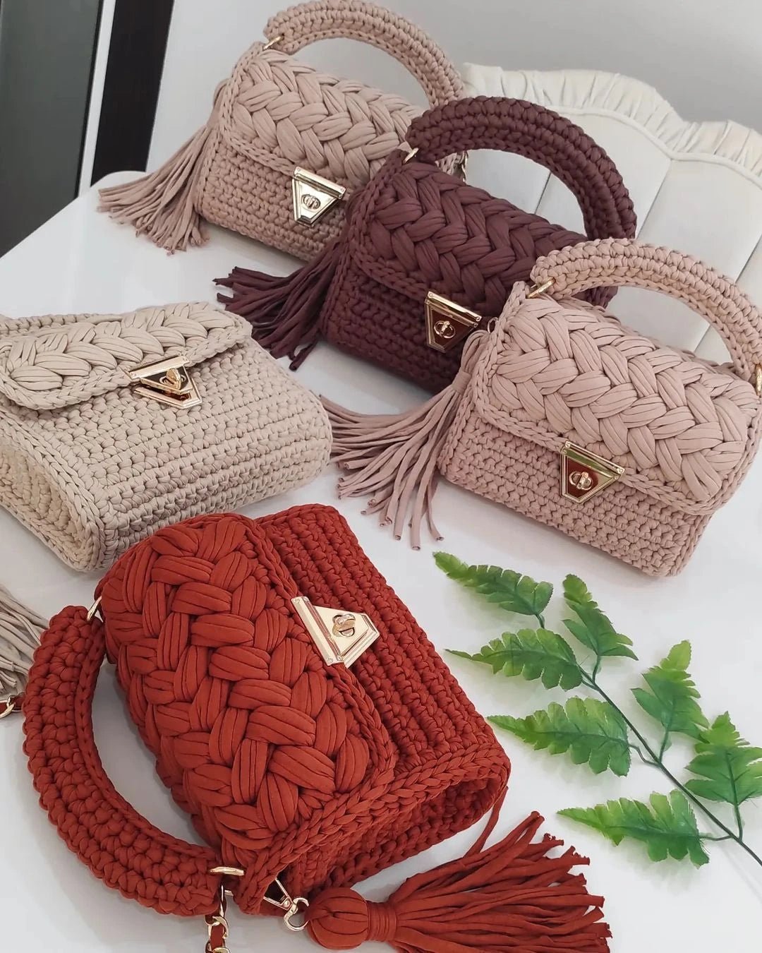 Set of woven handbags in various colors on a white surface with green leaves.